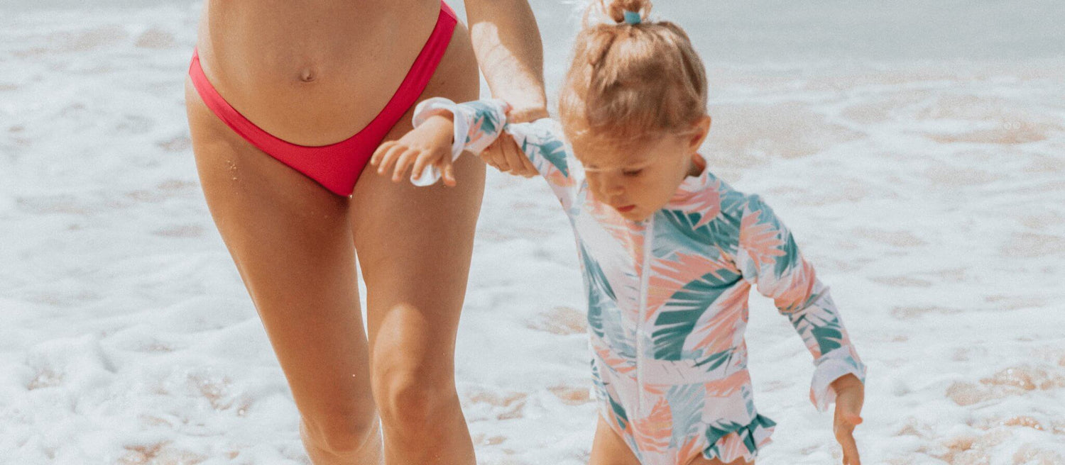 Little girl wearing a Midori Lil Babes swimsuit on the beach, showcasing adorable, comfortable, and protective kids’ swimwear.