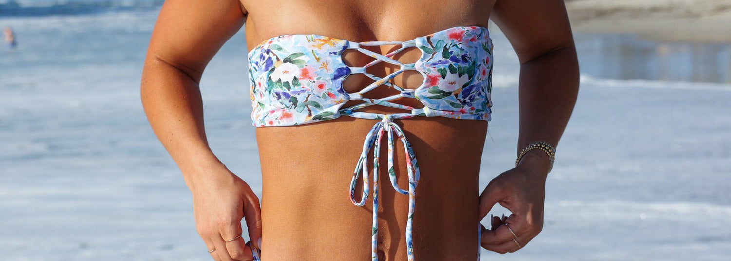 Assortment of Midori Bikinis' Swami strapless bandeau bikini tops in various vibrant prints, showcasing adjustable lace-up backs and sustainable swimwear.​